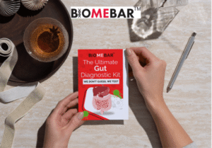 Person holding BiomeBar Ultimate Gut Diagnostic Kit with red packaging on a beige table, next to a drink, pen, and ribbon. Text on kit reads: 'We don’t guess, we test.' Perfect for promoting gut health testing and precision probiotics.